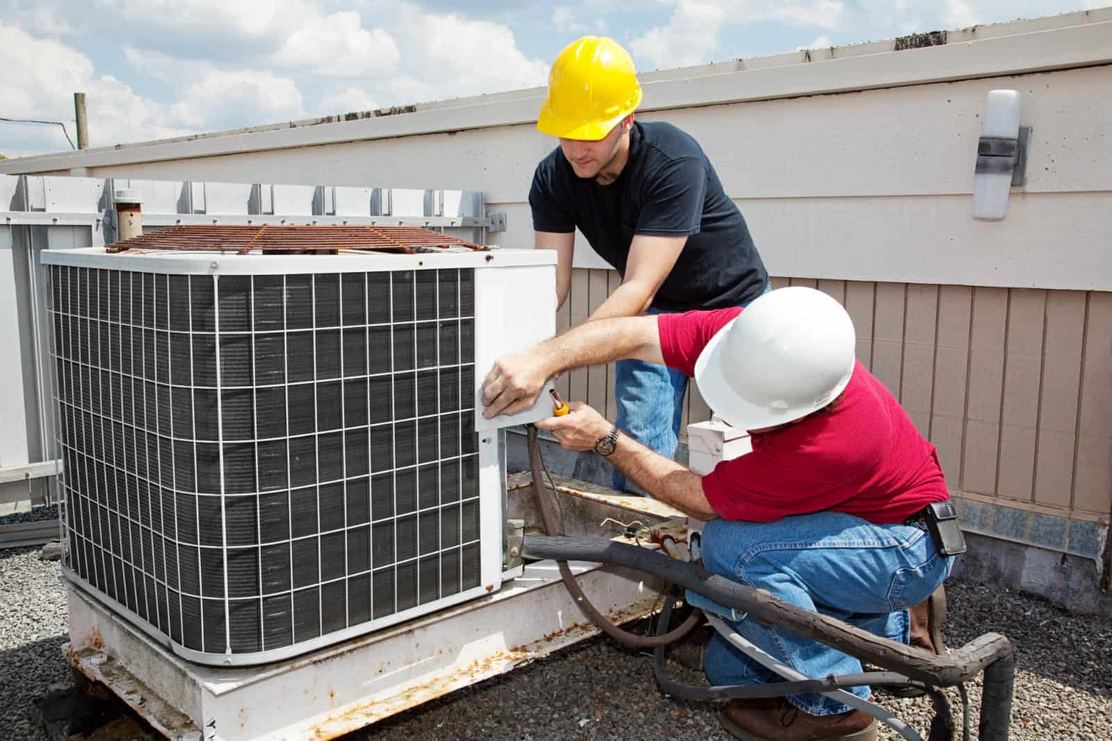 two hvac technicians working on a rooftop AC unit