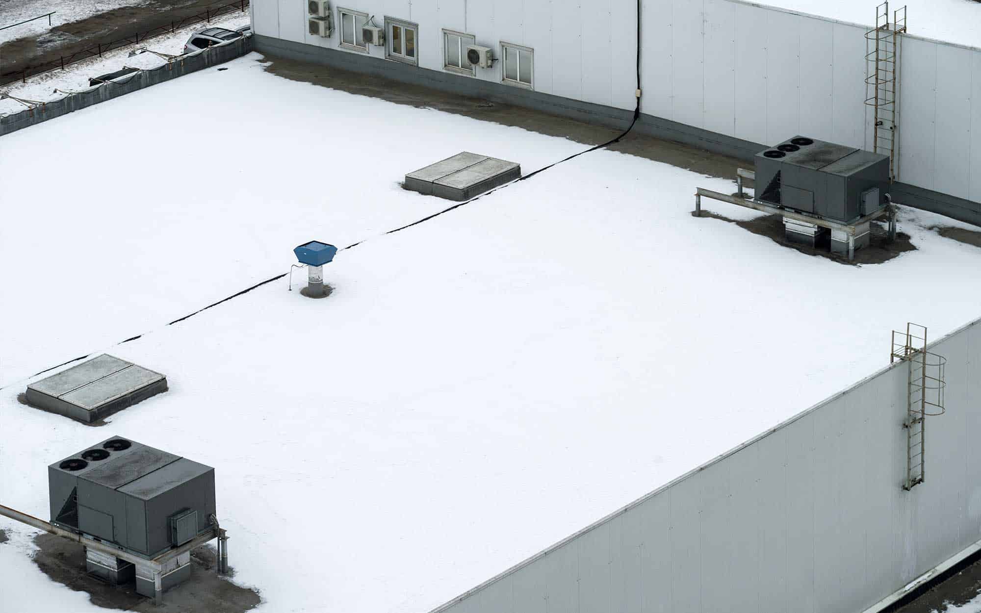 roof covered in snow with HVAC units on top of it