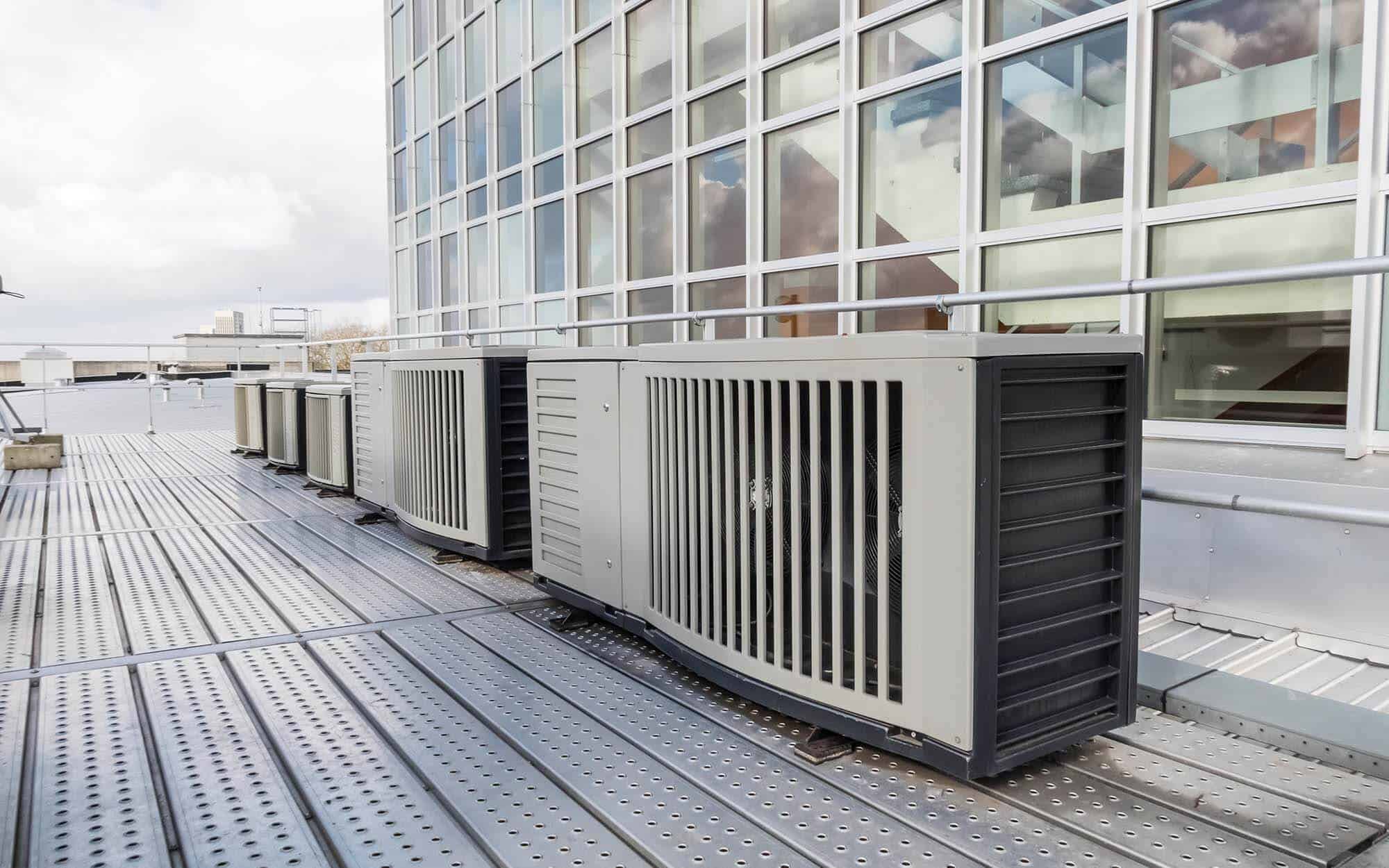 commercial HVAC units on a roof with windows behind them