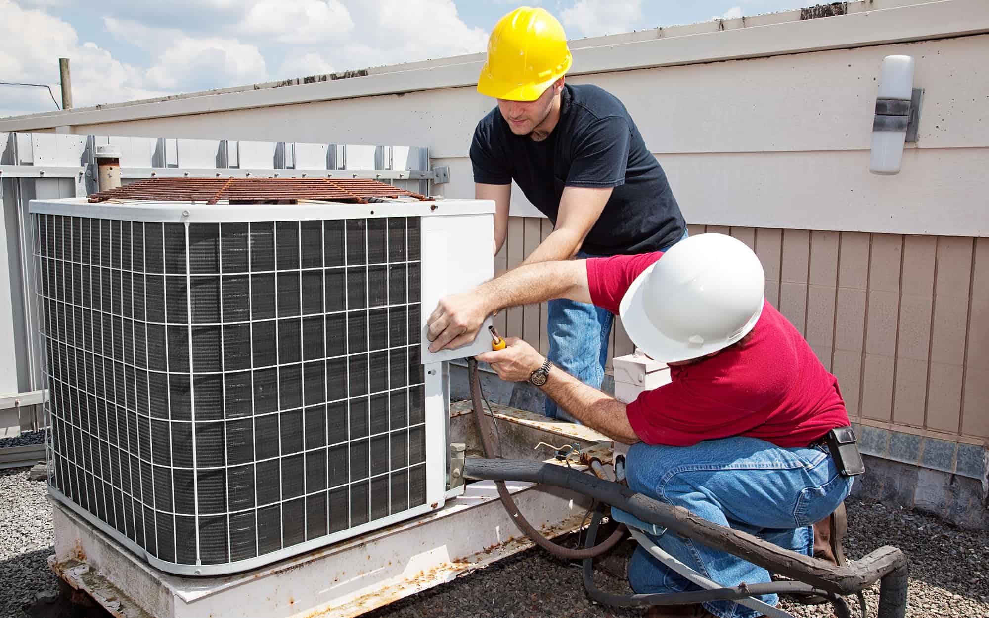 two hvac technicians working on a rooftop AC unit